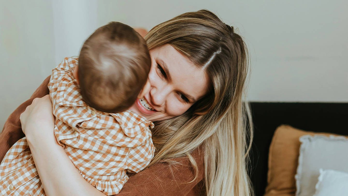 En kvinne vugger kjærlig en baby på en koselig seng, og viser frem et ømt øyeblikk mellom mor og barn.