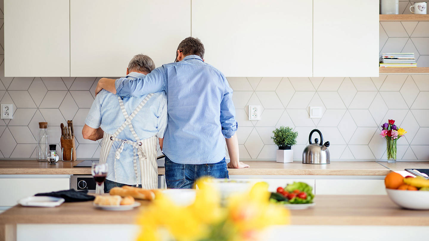 Far og sønn på et kjøkken med ryggen til