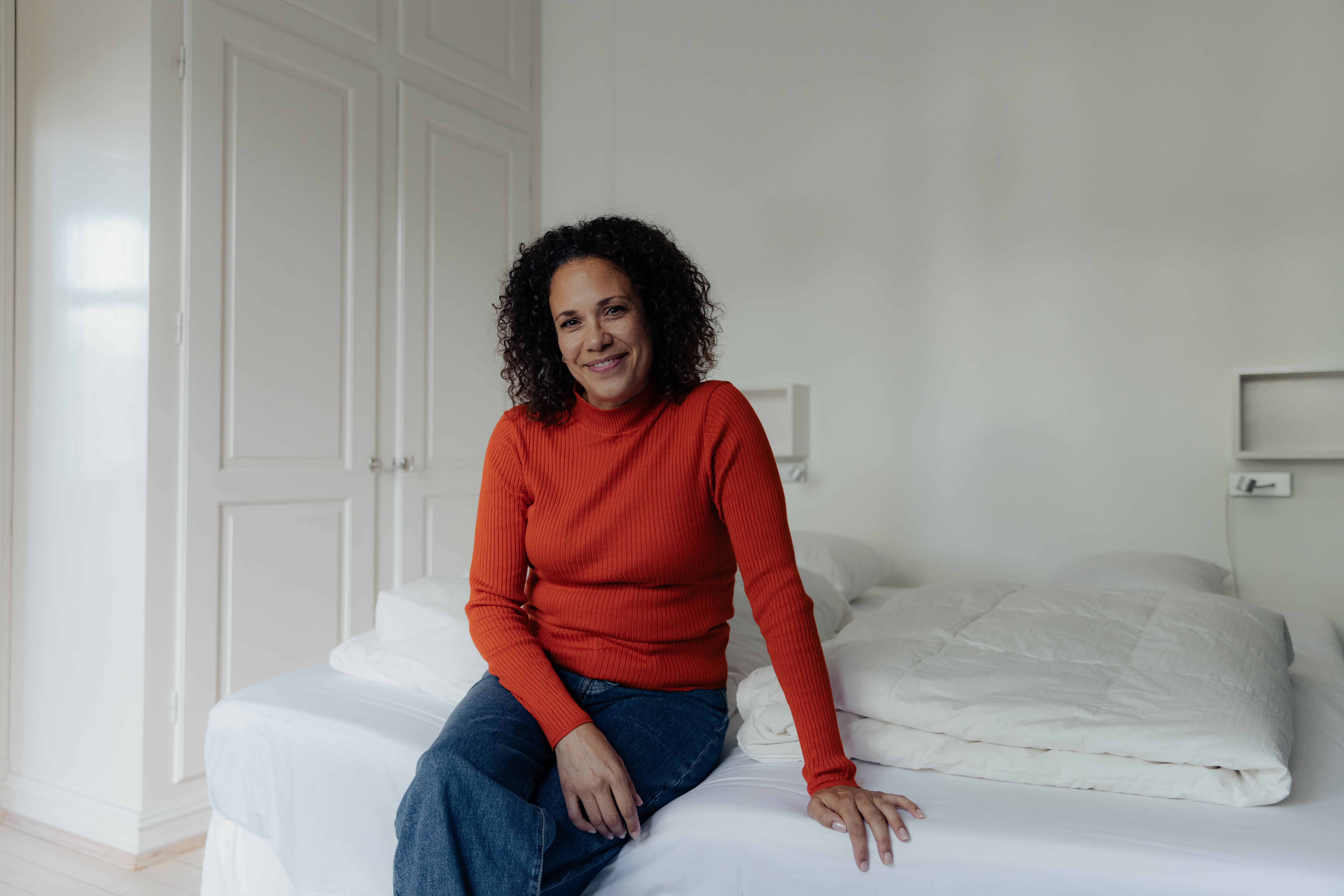 Kvinne sitter smilende på sengen